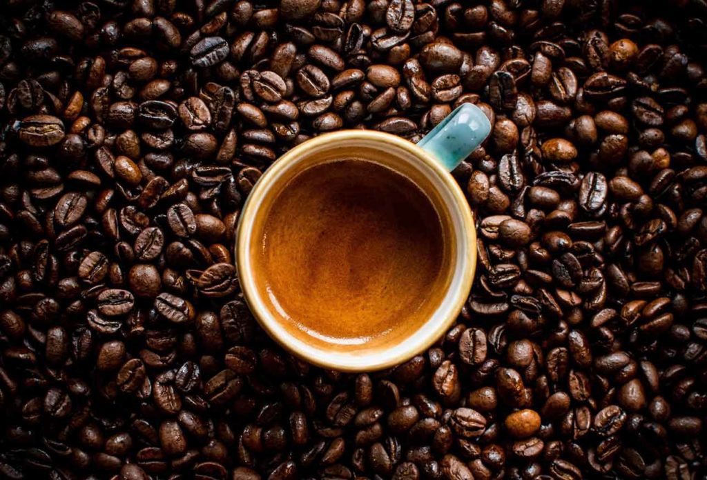 A shot of espresso sits in a pile of coffee beans